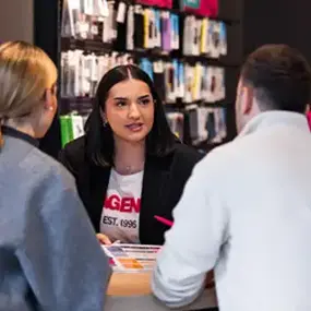 Beratungsgespräch im Handyshop: Verkäuferin zeigt Smartphone-Zubehör am Tresen
